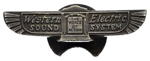 obverse: Medaglie Estere – Stati Uniti d’America (USA) – Western Electric - RR. Distintivo per abiti civili con piedino per asola di giacca emesso per pubblicizzare la società Western Electric in uso dal 1929 al 1958. Al dritto logo pubblicitario aziendale con scritta WESTERN ELECTRIC SOUND SYSTEM centralmente THE VOICE OF ACTION. Al rovescio sul piedino due punzoni. Realizzata in Argento 935% (AG) (6,5x27mm, 2,29 gr). Conservazione SPL. Molto Raro (RR). La Western Electric Company è stata un industria statunitense di prodotti elettronici per la telefonia, fondata nel 1869. Per buona parte della sua storia è stata una società completamente controllata dalla AT&T, per la quale produceva il materiale necessario all esercizio telefonico, dal 1881 al 1984, quando è stata smembrata