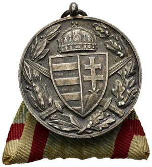 obverse: Medaglie Estere – Ungheria – Prima Guerra Mondiale – WW1. Decorazione dell’Ungheria per i soldati partecipanti alla Prima Guerra Mondiale (WW1). Emessa nel 1920. Al dritto stemma ungherese sormontato dalla Sacra Corona e sovrapposto a due spade decussate tra rami di alloro e quercia. Al rovescio PRO DEO ET PATRIA. Elmetto d’assalto sotto 1914-1918 tra due rami di palma. Coniata in Bronzo argentato (AE) (ø 36.4mm, 24.1g). Scritta BRONZ sul bordo. Nastrino d’epoca. Conservazione SPL. Riferimenti Barac 45.