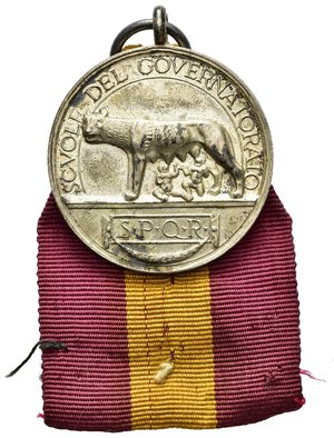 obverse: Medaglie Italiane – Regno d’Italia - Vittorio Emanuele III (1900-1945) – Ventennio Fascista – Scuole Governatorato - Roma. Medaglia premio, portativa con appiccagnolo ed anello, commemorante il merito. Al dritto lupa capitolina su basamento verso s. sotto Romolo e Remo, in basso scritta S.P.Q.R, entro cartella e festone, in alto SCVOLE DEL GOVERNATORATO. Al rovescio entro ghirlanda un fascio littorio e A.VII (1929-1930) sopra scritta AL MERITO. La medaglia realizzata in argento (AG) (Ø 30.3mm, 13.2g.). Conservazione BB. Con nastrino rosso giallo rosso originale d’epoca. Riferimenti Casolari VII-15