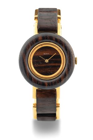 obverse: Gucci Wood, anni 70 Cassa rotonda in legno e oro 18k. Quadrante in legno. Movimento a carica manuale. Bracciale in legno e oro 18k. Dimensioni: 33 mm. Accompagnato da scatola d epoca Gucci.